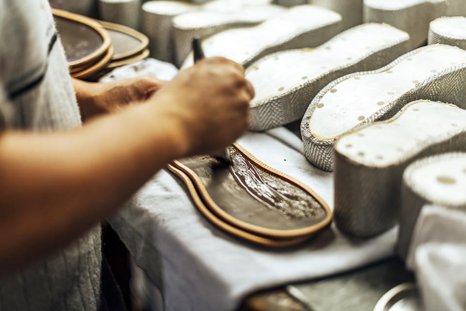 Hands of an old and experienced worker in the handmade footwear industry, performing sole gluing tasks, putting glue on the base of the shoe.